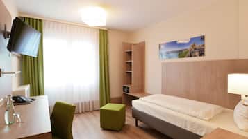 A hotel room with a bed, a desk, a chair, a TV, a painting, and a window with curtains.