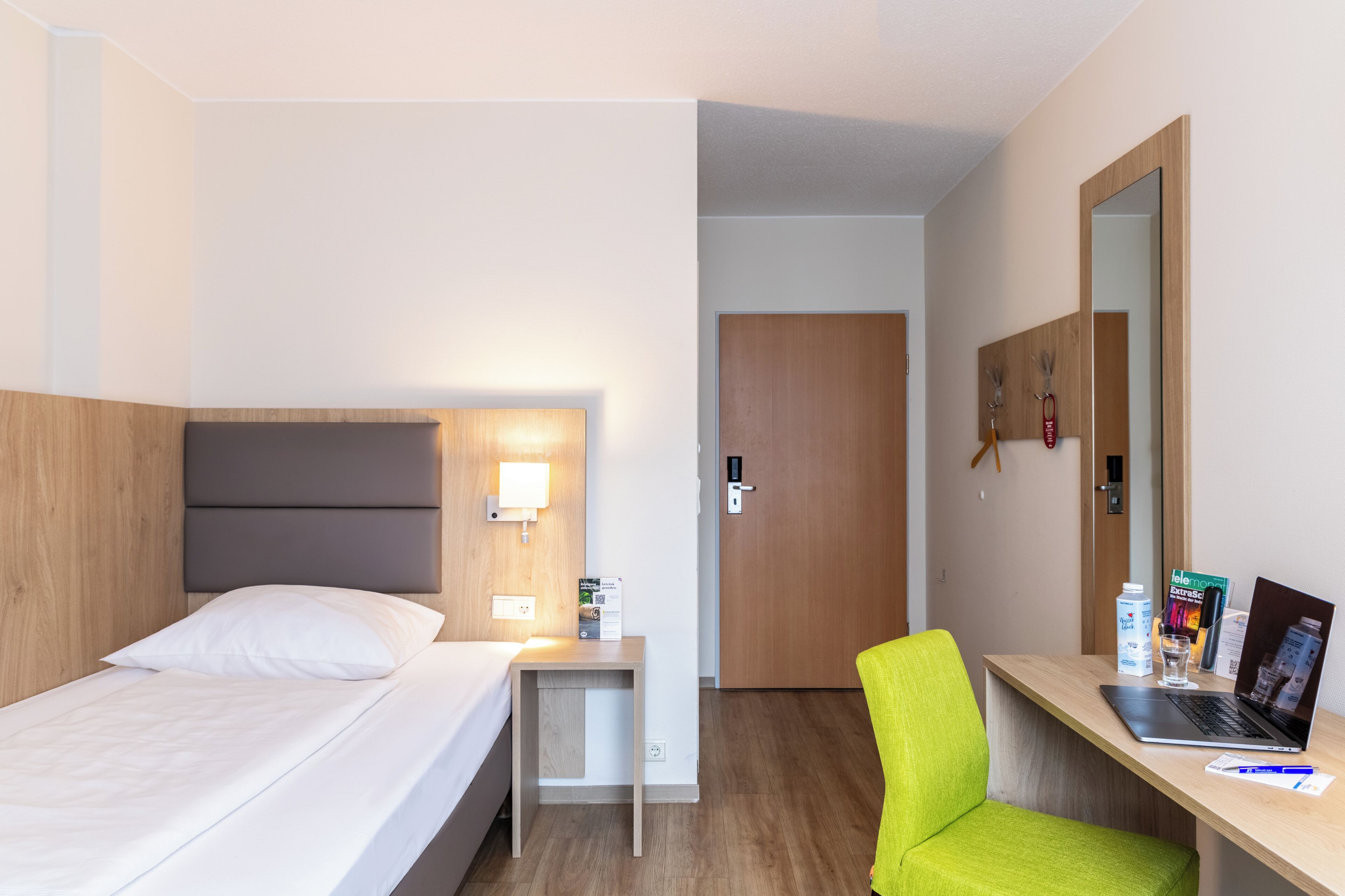 Une chambre d’hôtel comprenant un lit, une table de chevet, une chaise, un bureau avec un ordinateur portable et un miroir.