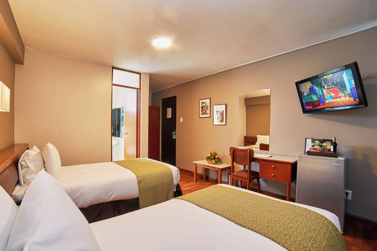 Ein Hotelzimmer mit zwei Betten, einem Schreibtisch, einem Sessel, einem Fernseher und einer Minibar.