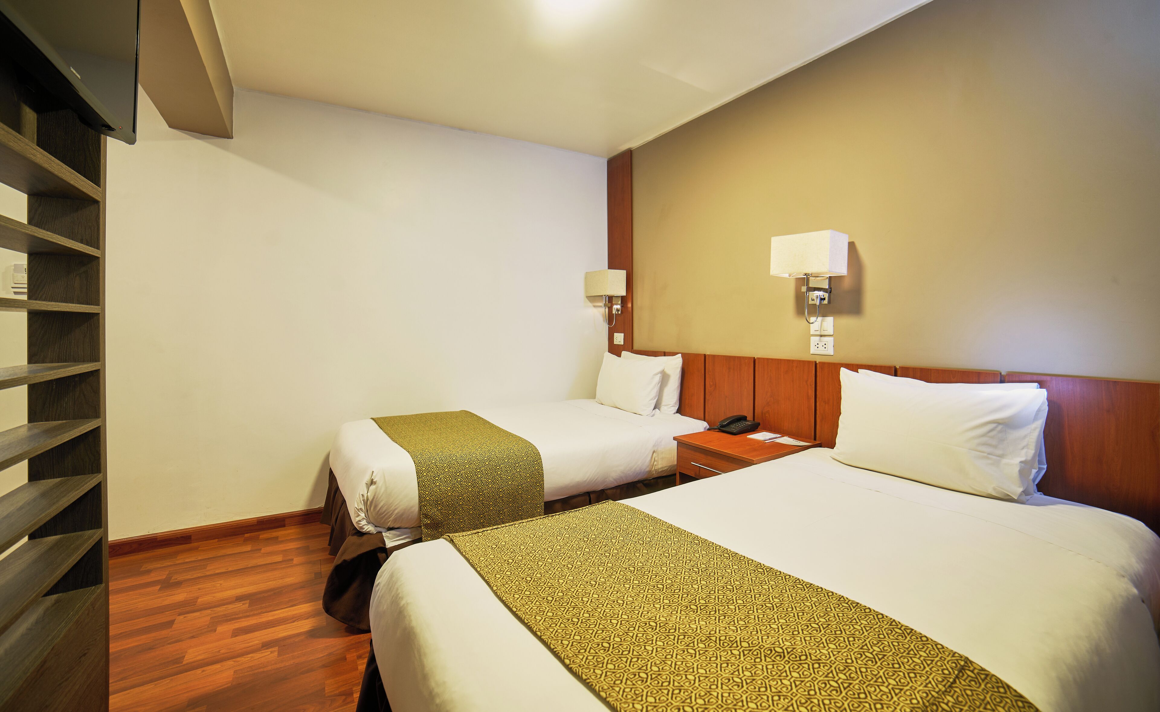 Habitación de hotel con dos camas, suelo de madera, una mesita de noche con teléfono y una lámpara de pared.
