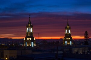 Two illuminated church towers against a sunset sky.