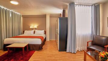 Una habitación de hotel con cama, escritorio, silla, cómoda y ventana con cortinas.
