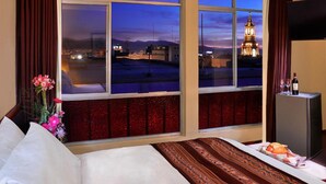 Une chambre d’hôtel dotée d’une grande fenêtre donnant sur un paysage urbain et sur un bâtiment imposant, au crépuscule.