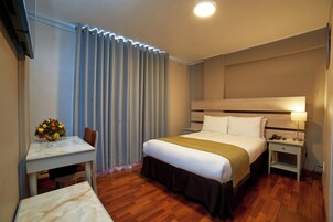 Una habitación de hotel con una cama, mesita de noche, lámpara y un escritorio con una silla y un jarrón de flores.