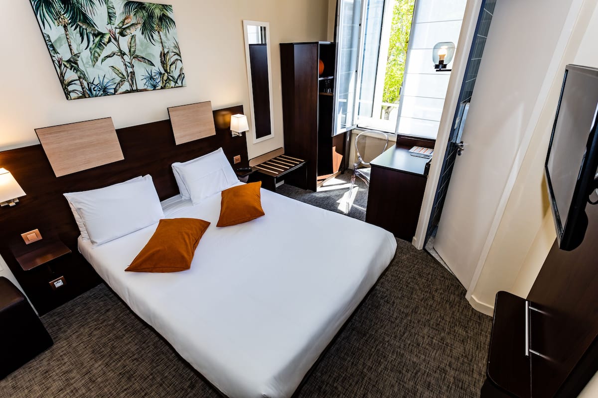 Une chambre d’hôtel avec un grand lit, un bureau, une chaise, une télévision et une fenêtre donnant sur un paysage verdoyant.