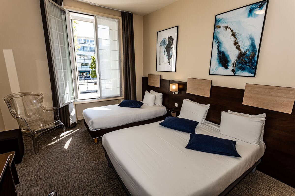 Une chambre d’hôtel avec deux lits, une chaise et des œuvres d’art accrochées aux murs.