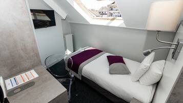 A compact hotel room with a bed, a bedside table, a TV mounted on the wall, and a skylight.