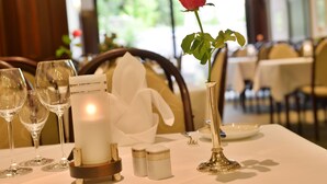 Une table à manger dressée avec des verres à vin, une bougie, des salières et des poivrières, une rose dans un vase et un porte-serviettes blanc.