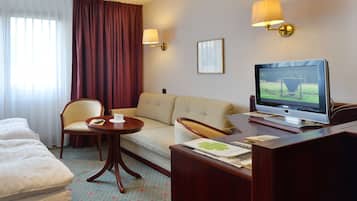Une chambre d’hôtel comprenant un lit, un canapé, un bureau avec un ordinateur, une petite table avec une télécommande et un téléviseur.