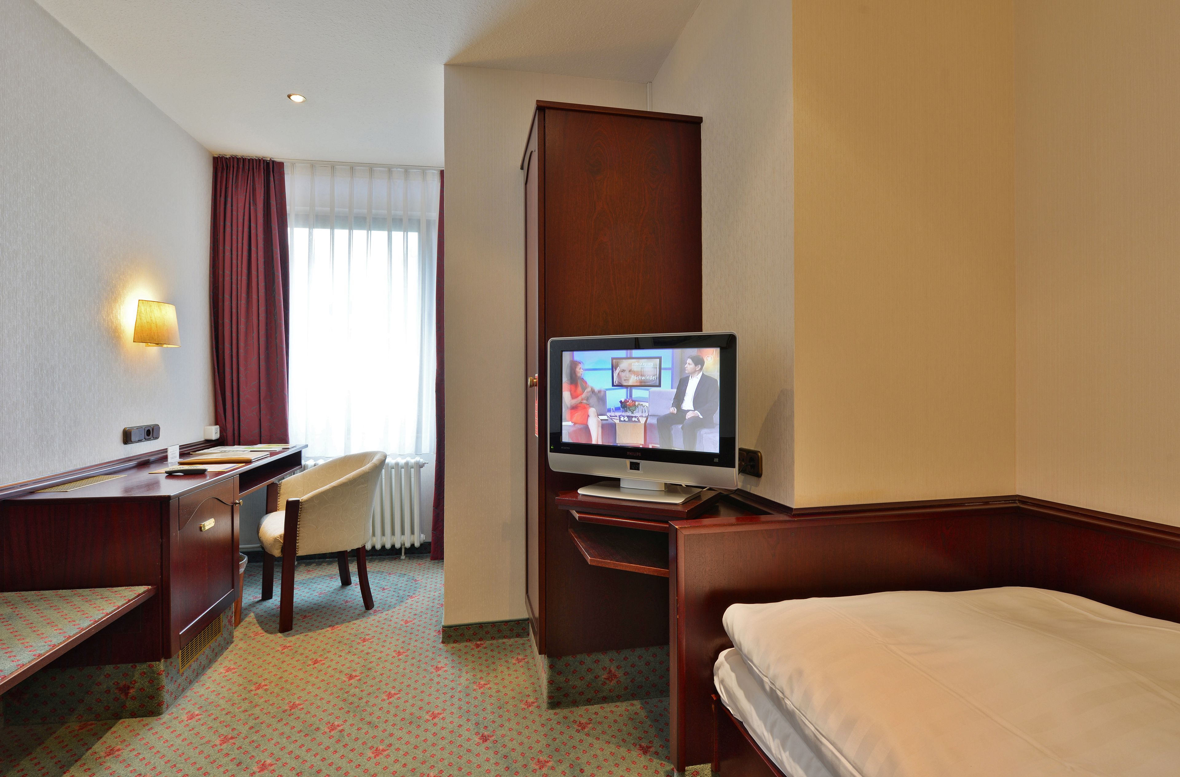 A hotel room with a bed, desk, chair, television, and a window with curtains.