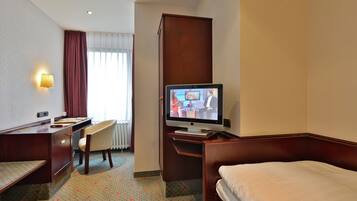 Una habitación de hotel con cama, escritorio, silla, televisor y ventana con cortinas.