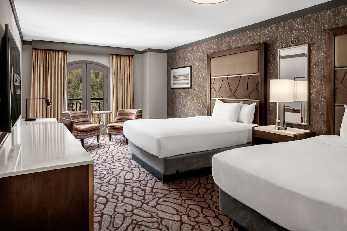A hotel room with two beds, a desk, a chair, a TV, and a window with curtains.