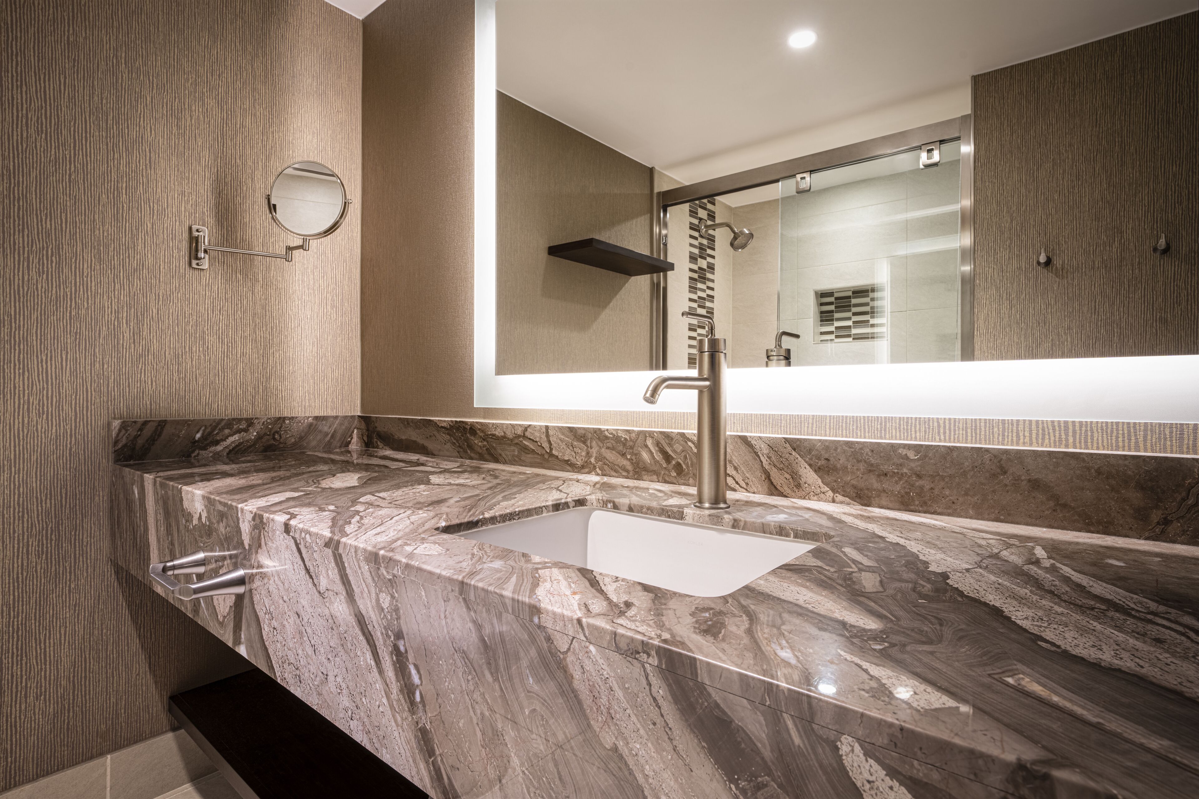 Een moderne badkamer met een marmeren aanrechtblad, een spiegel aan de muur en een douchehoek.