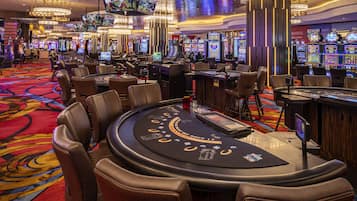Un salón de casino con varias mesas de juego, máquinas tragamonedas y una pantalla grande mostrando un evento deportivo.