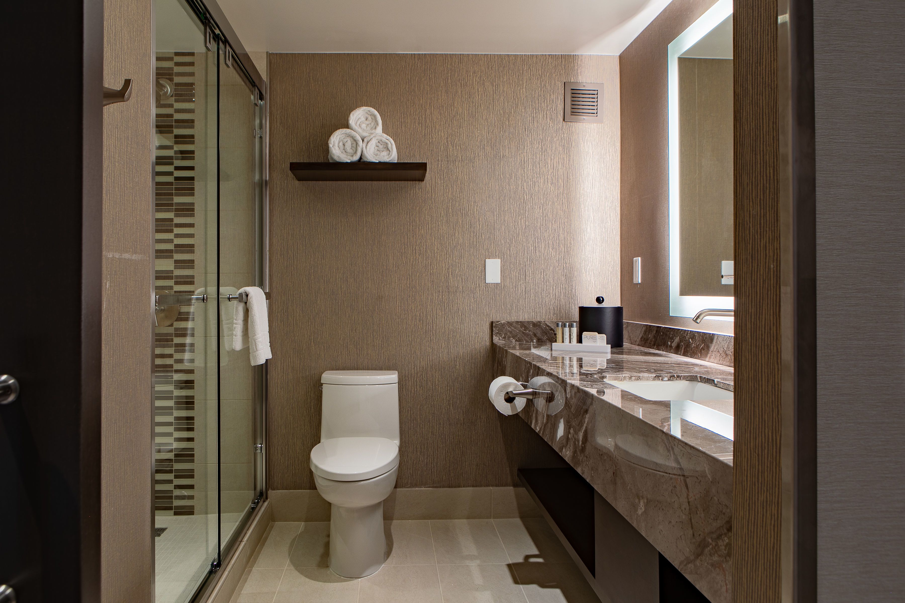 Een moderne badkamer met een glazen douchecabine, een toilet, een marmeren wastafel en een handdoekrek met handdoeken.