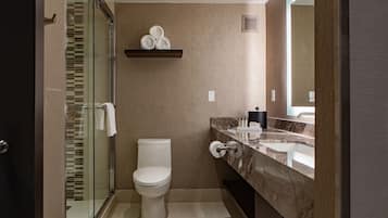 Een moderne badkamer met een glazen douchecabine, een toilet, een marmeren wastafel en een handdoekrek met handdoeken.