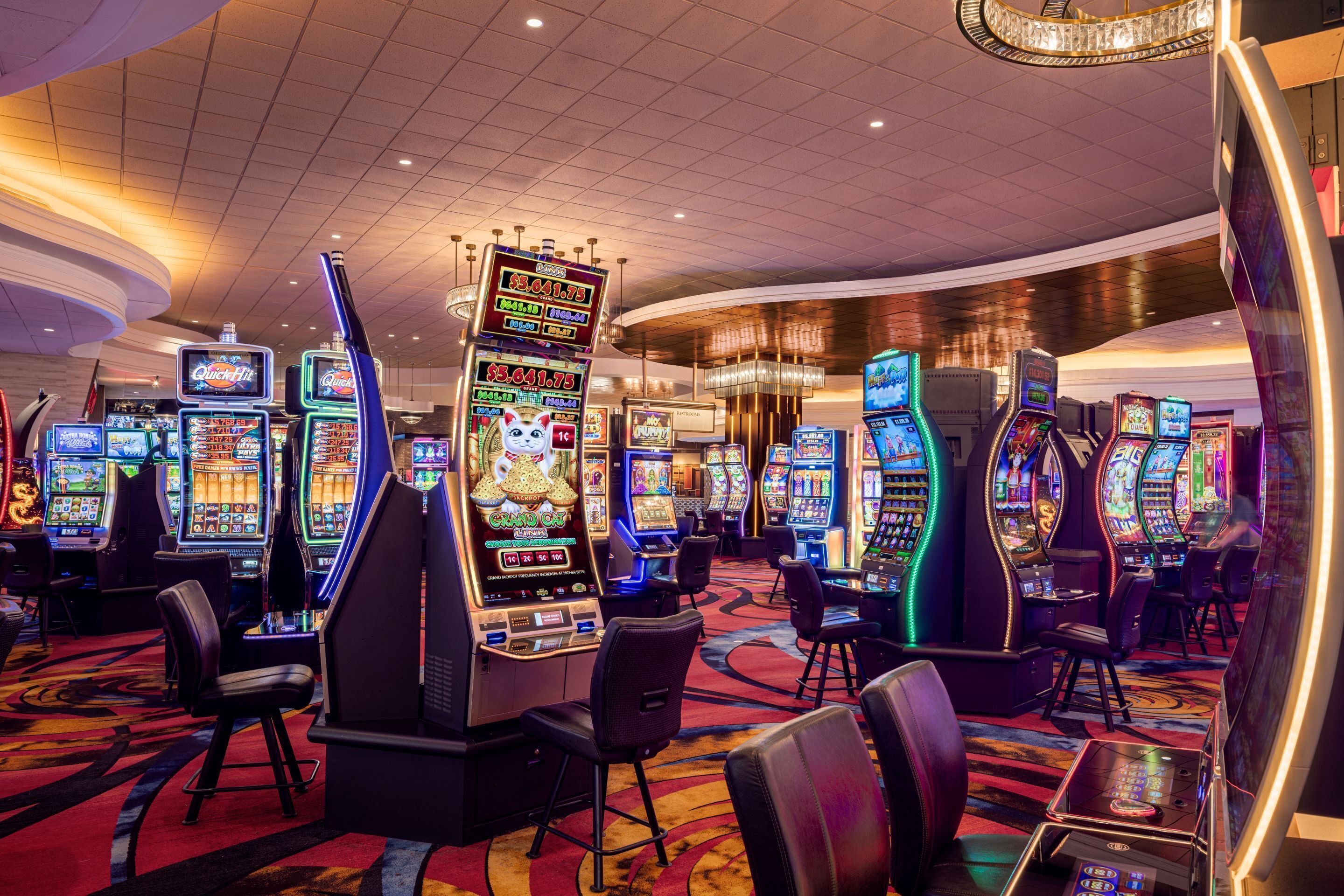 A casino with multiple slot machines and gaming tables, arranged in rows with chairs in front.