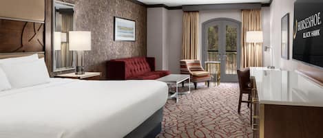 Habitación de hotel con una cama grande, un sofá rojo, una mesita, una silla, un escritorio y un televisor.