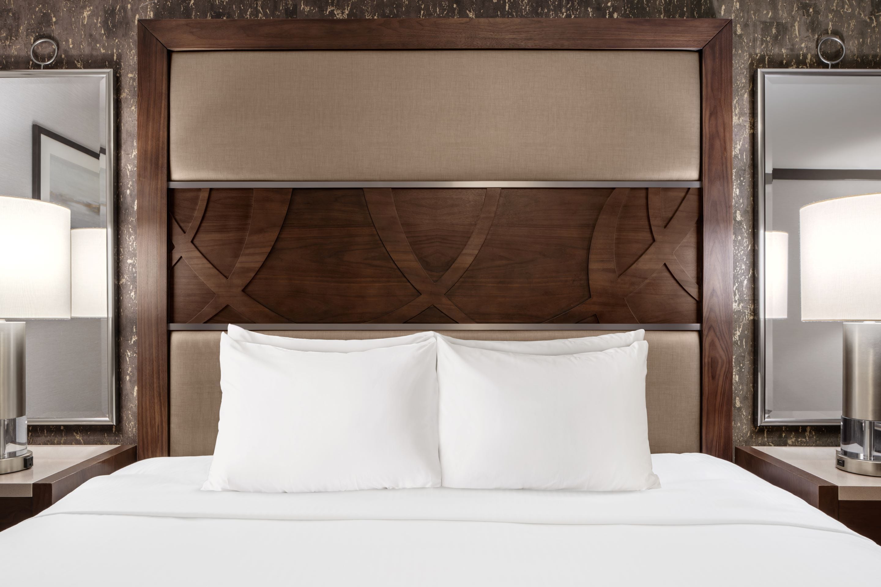 A neatly made bed with white linens and a wooden headboard with a geometric design.