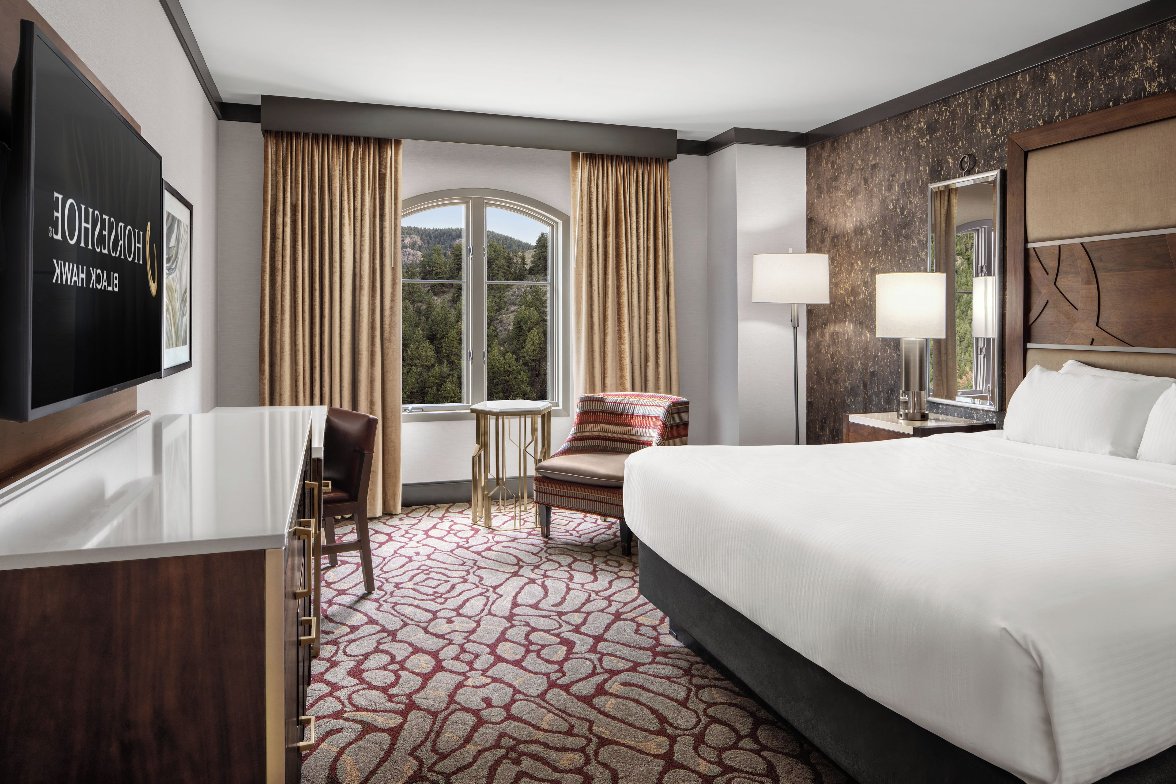 Habitación de hotel con cama, escritorio, silla, mesa y ventana con cortinas.