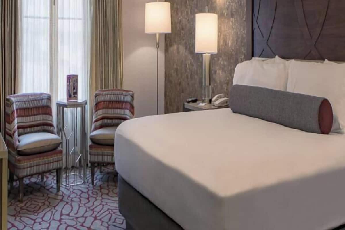 A hotel room with a large bed, two armchairs, a small table, and two bedside lamps.