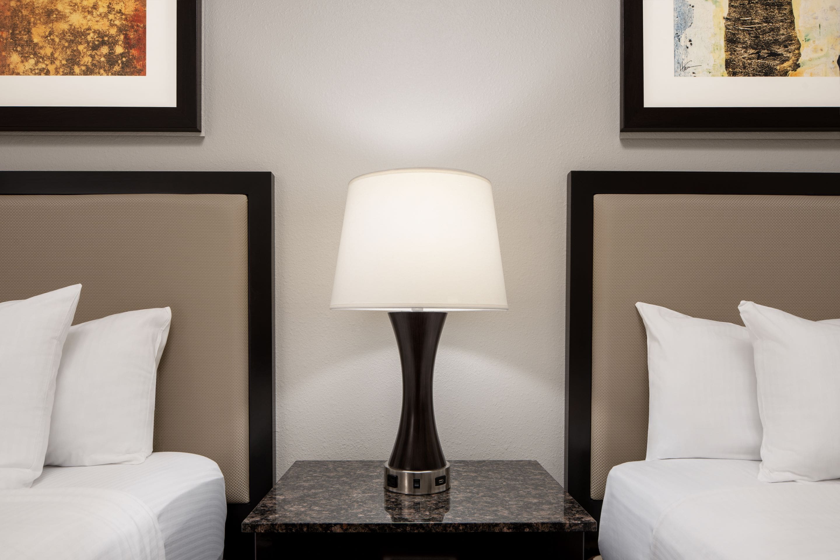 Een hotelkamer met twee bedden, een nachtkastje met een lamp en lijstwerken aan de muur.