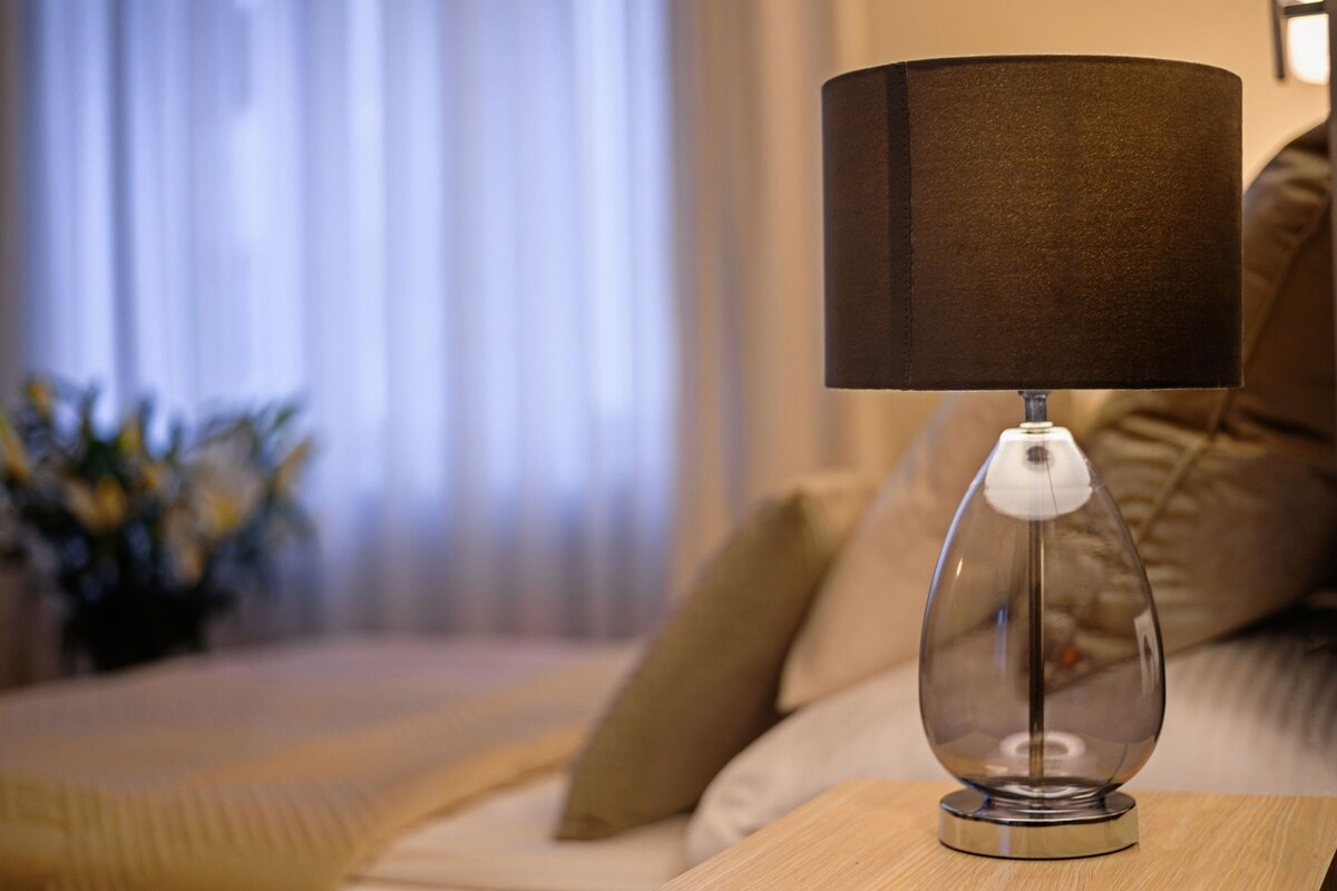 Una lámpara con pantalla de vidrio transparente sobre una mesita de noche de madera en una habitación de hotel.