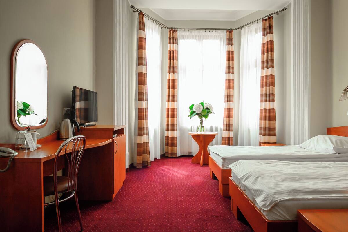 Une chambre d’hôtel équipée d’un bureau, d’une chaise, de deux lits, d’une petite table avec une plante et d’un téléviseur.