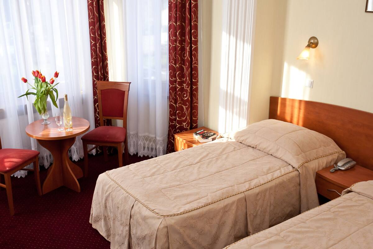 Une chambre d’hôtel avec deux lits, une petite table ornée d’un vase de fleurs, une chaise et une table de chevet avec une lampe.