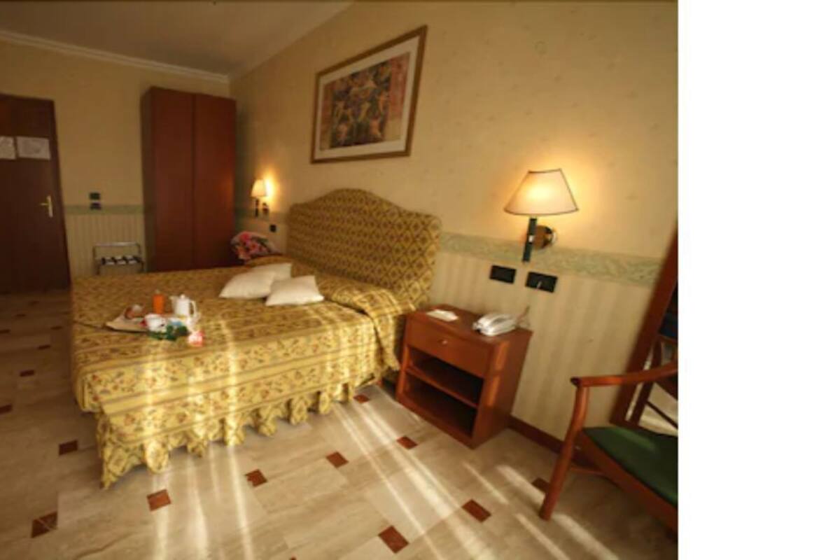 A hotel room with a bed, bedside table, lamp, and a door leading to another room.