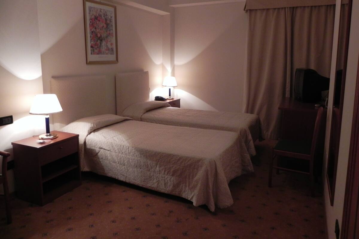 A hotel room with two beds, a desk with a lamp, a chair, and a television.
