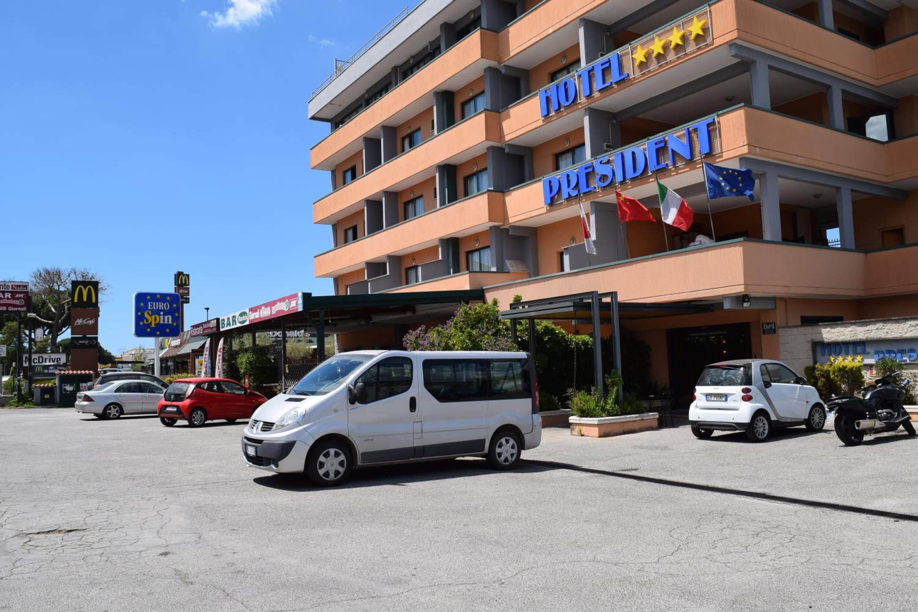 A multi-story hotel with a prominent "HOTEL PRESIDENT" sign, multiple balconies, and flags including the EU flag.