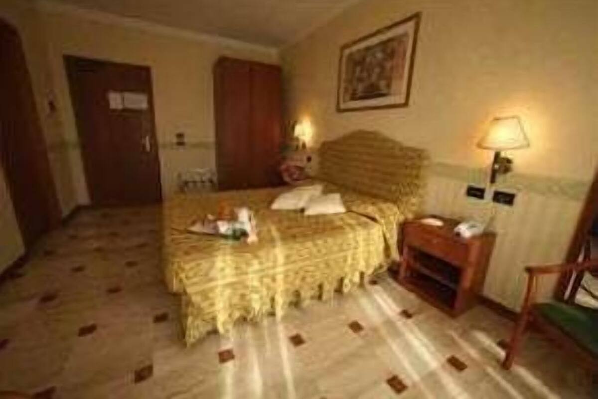 A hotel room with a bed, a nightstand, a chair, a door, and a wall-mounted lamp.