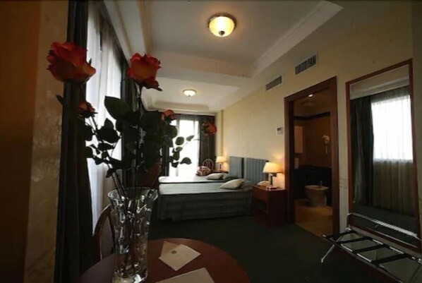 A hotel corridor with a bed, bedside table, lamp, and a window with curtains. - Hotel President Pomezia (Pomezia)