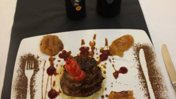 A dessert on a square plate with sauces and garnishes, accompanied by a fork and knife on a table.