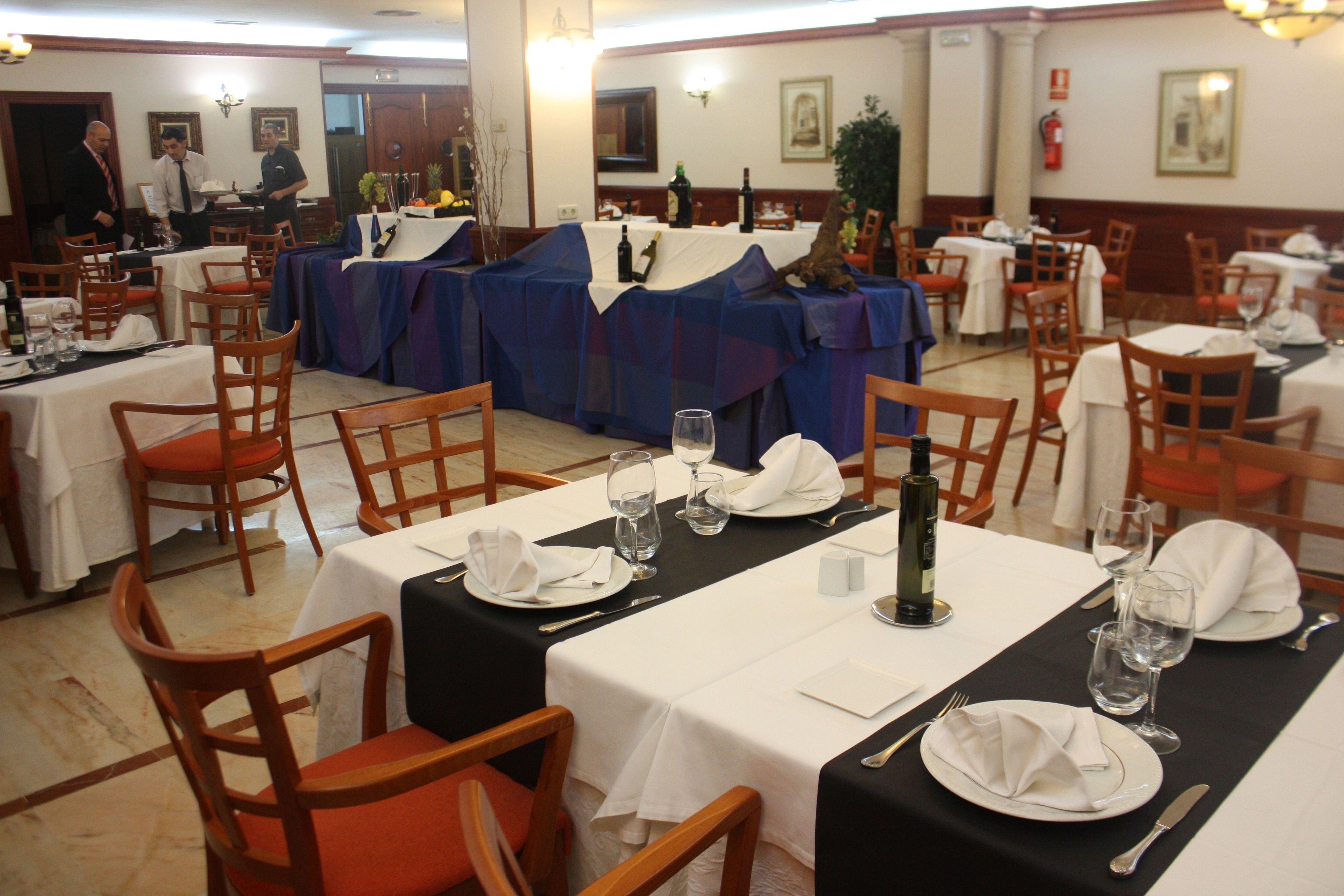 Un restaurante con mesas dispuestas para comer, sillas y un camarero al fondo.