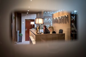 Uma mesa de recepção com acabamento em madeira, uma luminária de pé e um vaso com planta.