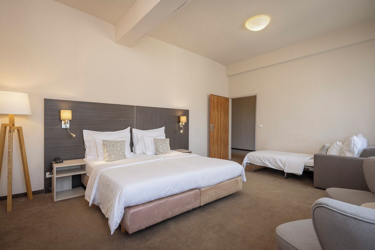 A hotel room with a large bed, bedside tables, a desk, a chair, and a sofa.