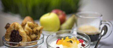 Ein Frühstückstisch mit Joghurt, Früchten, Samen, einer Kaffeetasse und einem Gebäckstück.