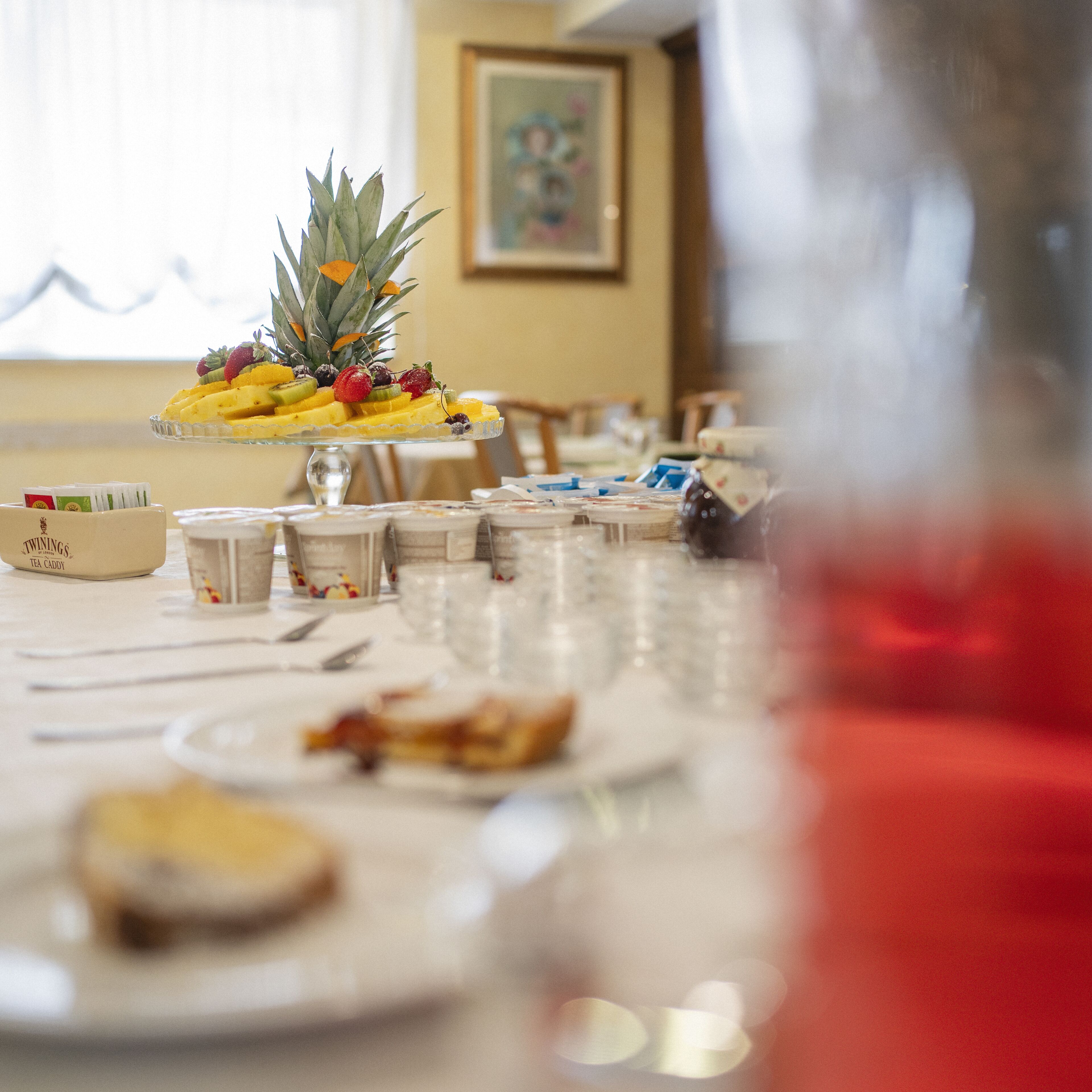 Une table à manger avec un plateau de fruits, une boîte à thé et divers récipients contenant de la nourriture.