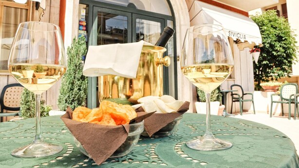 A table with two wine glasses, a gold pot, and bowls of snacks. - Hotel Siviglia (Fiuggi)