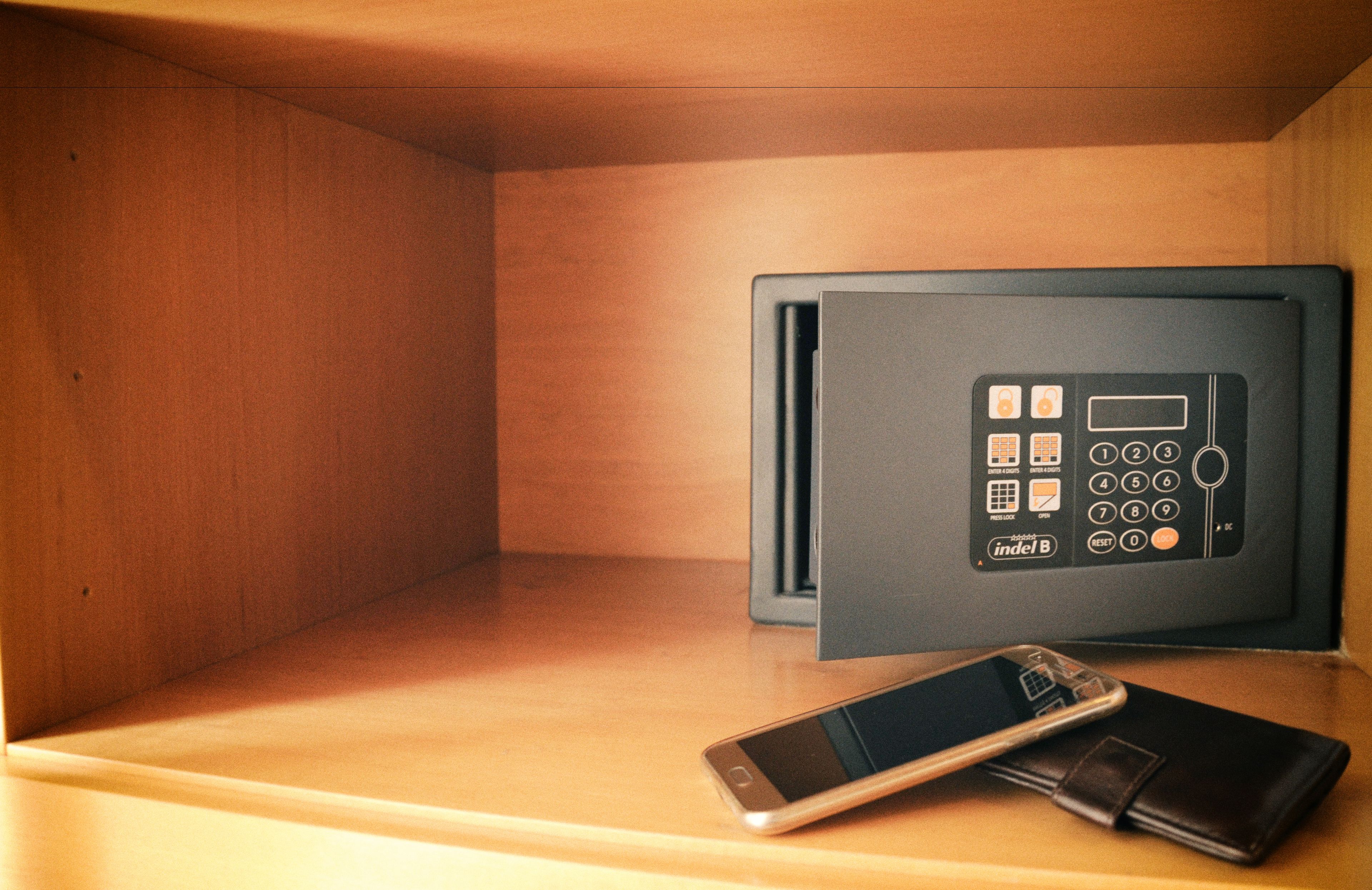 A safe deposit box with a keypad, a smartphone, and a wallet on a wooden surface.