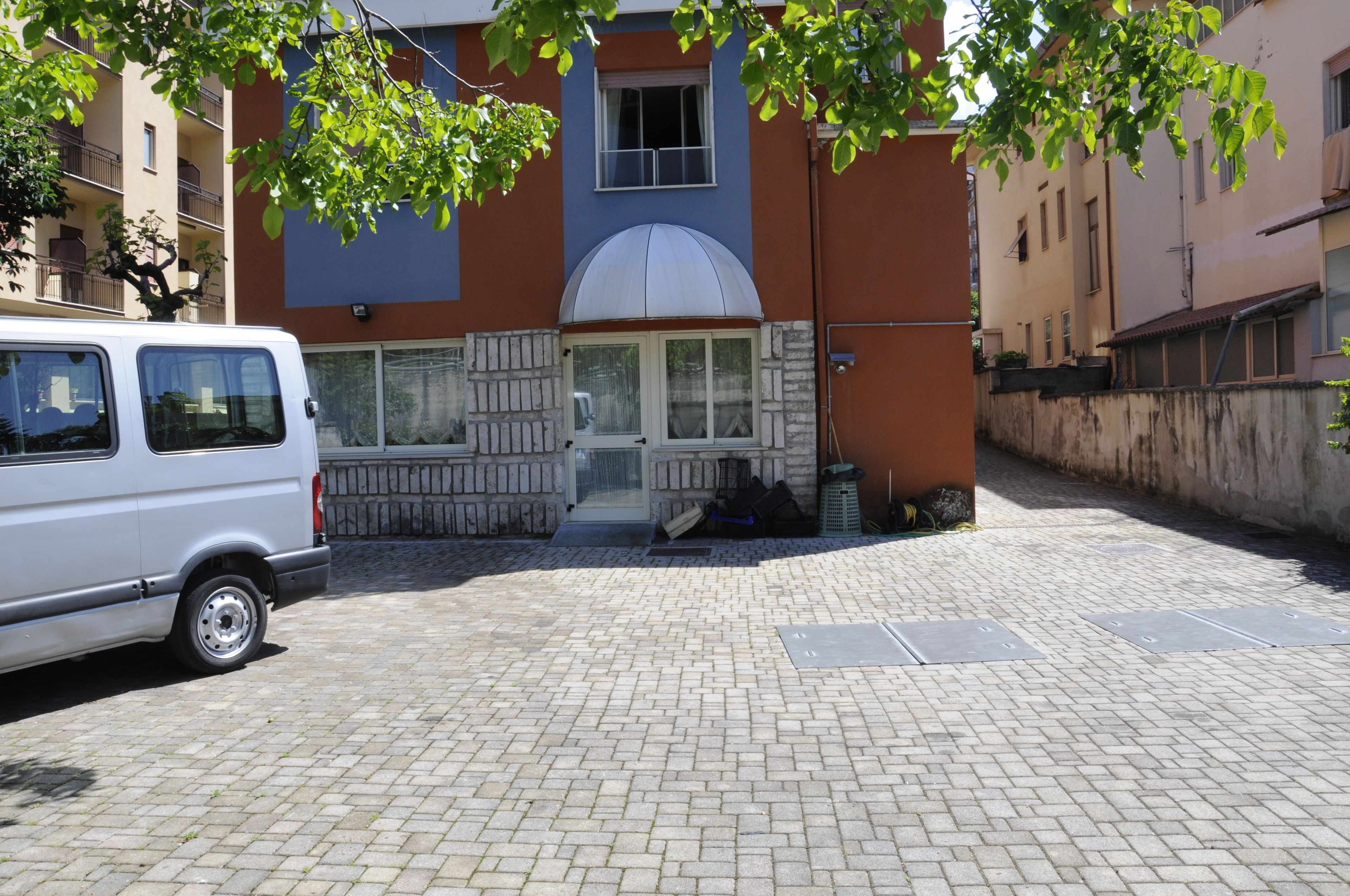 A white van parked in front of a building with a brick facade, a large window with a white frame, and a small door.