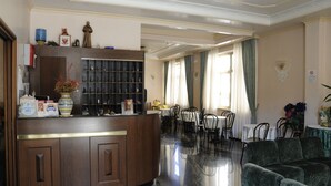 A hotel lobby with a reception desk, a dining area with tables and chairs, and a green sofa. - Hotel Siviglia (Fiuggi)