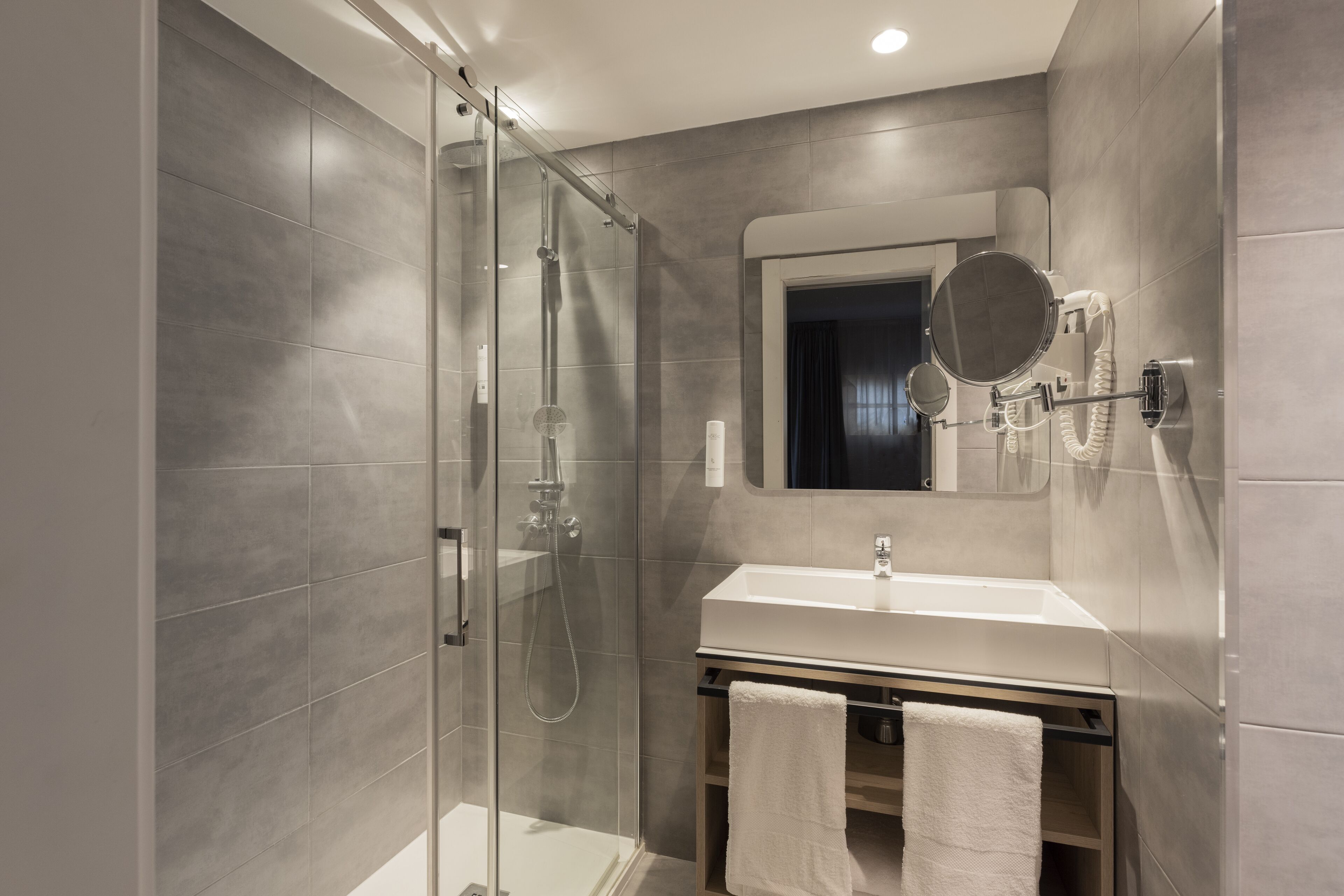 Une salle de bain moderne avec une douche à parois de verre, un lavabo blanc et un miroir doté d’un cadre rond.