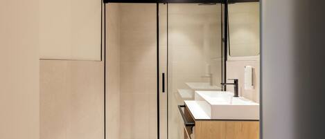 A modern bathroom with a glass-enclosed shower, a wooden vanity, and a large mirror.