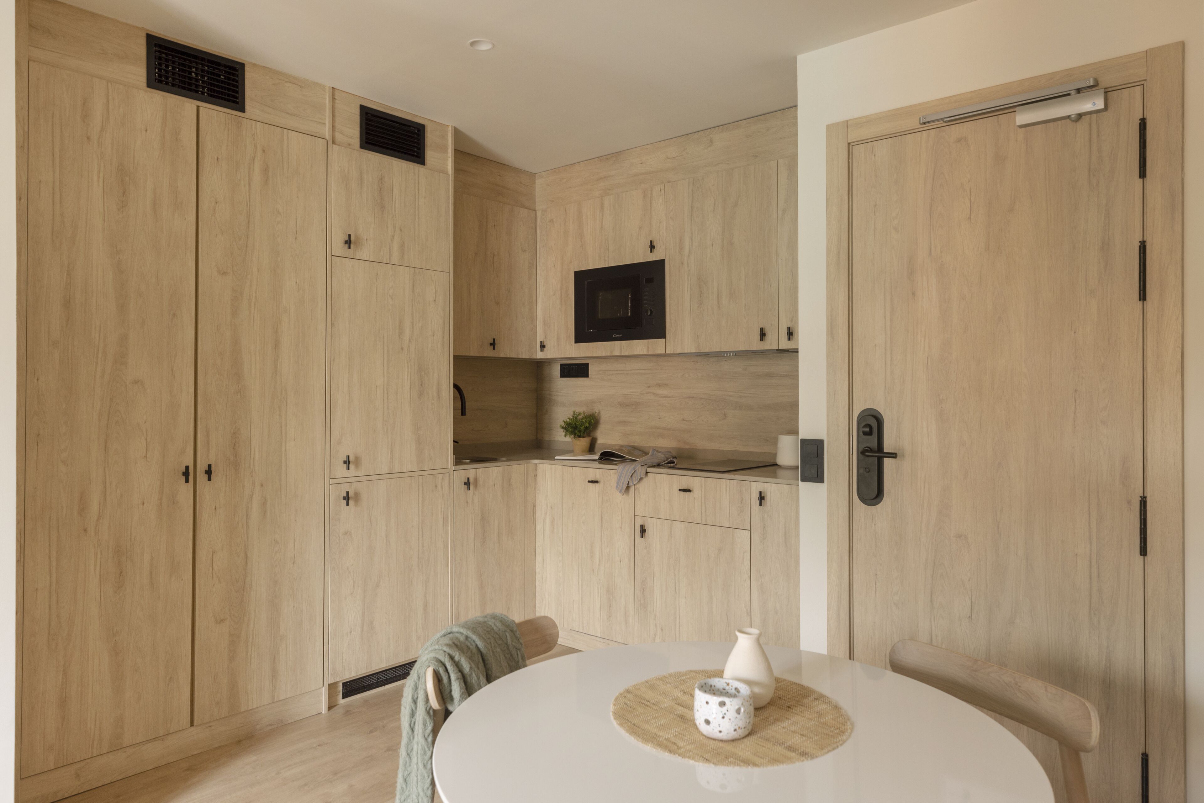 Una cocina moderna con armarios de madera, un microondas y una zona de comedor con una mesa redonda.