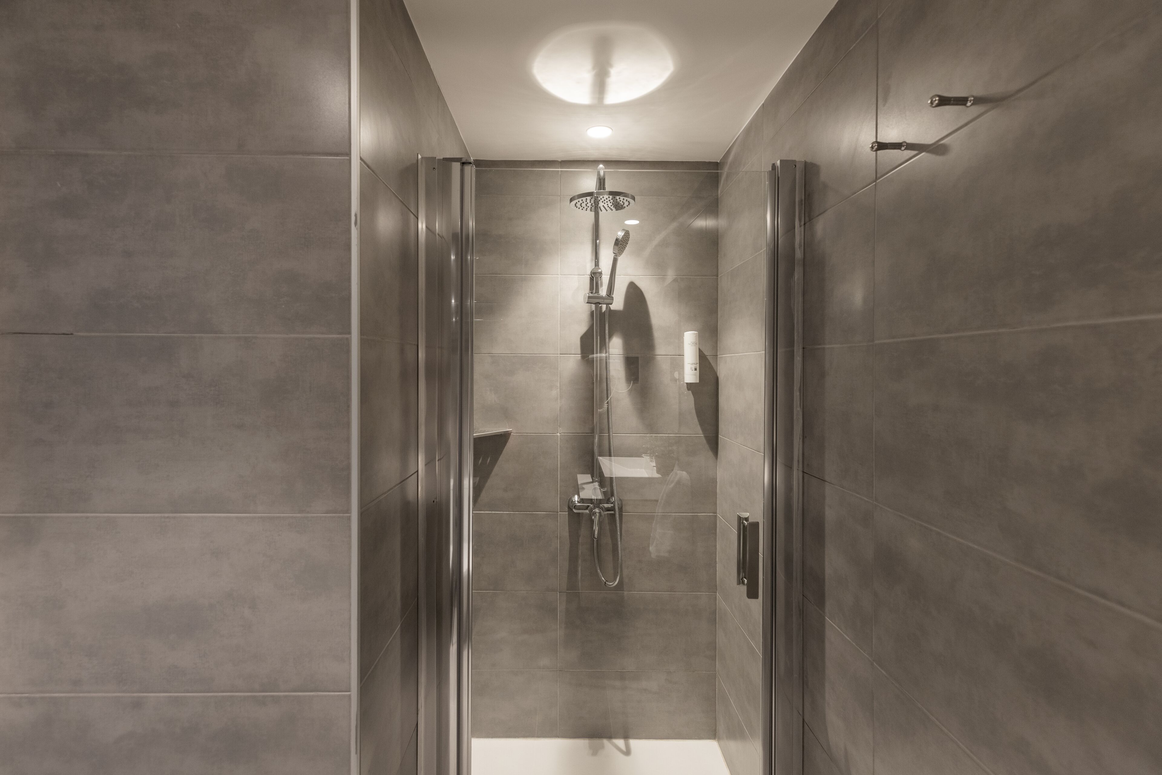 A modern shower with a glass door, a handheld showerhead, and a wall-mounted faucet.