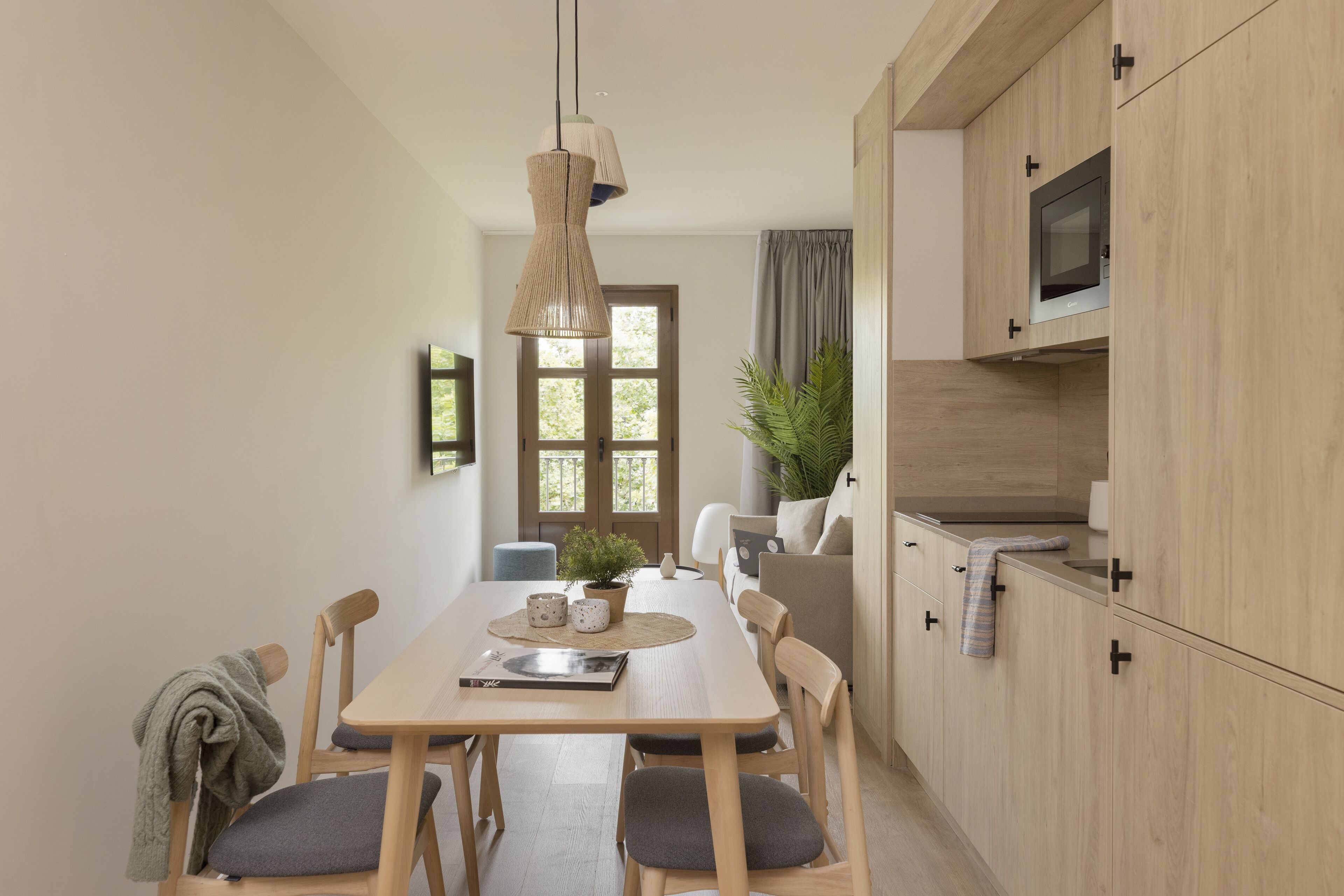A modern kitchen with wooden cabinets, a dining table with chairs, and a hanging light fixture.