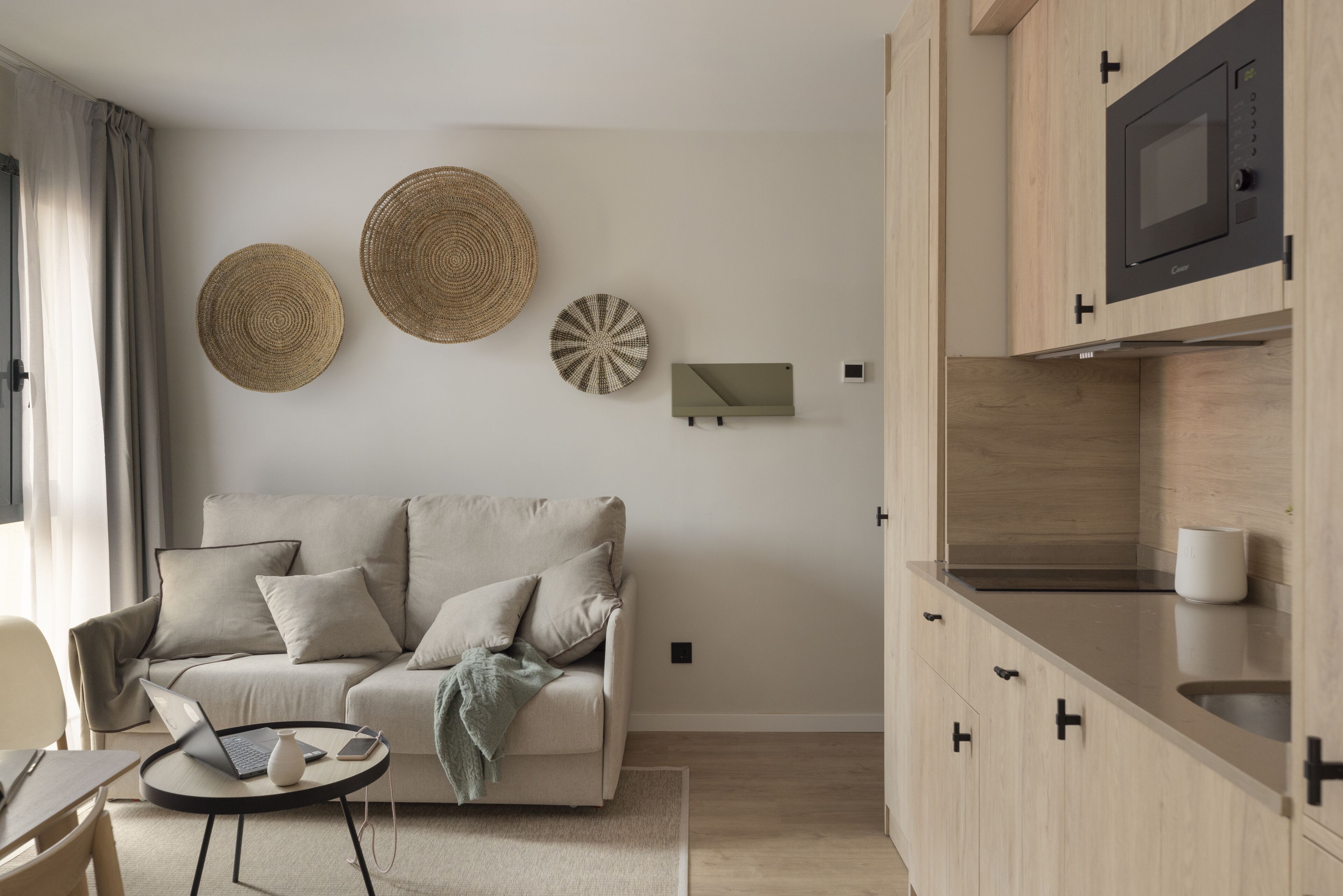 Een moderne woonkamer met een bank, een salontafel en een laptop. Er is een keukenhoek met een magnetron en kastjes.